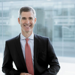 Businessportrait eines Geschäftsführers aufgenommen vor moderner Glasfassade, er lacht offen in die kamera
